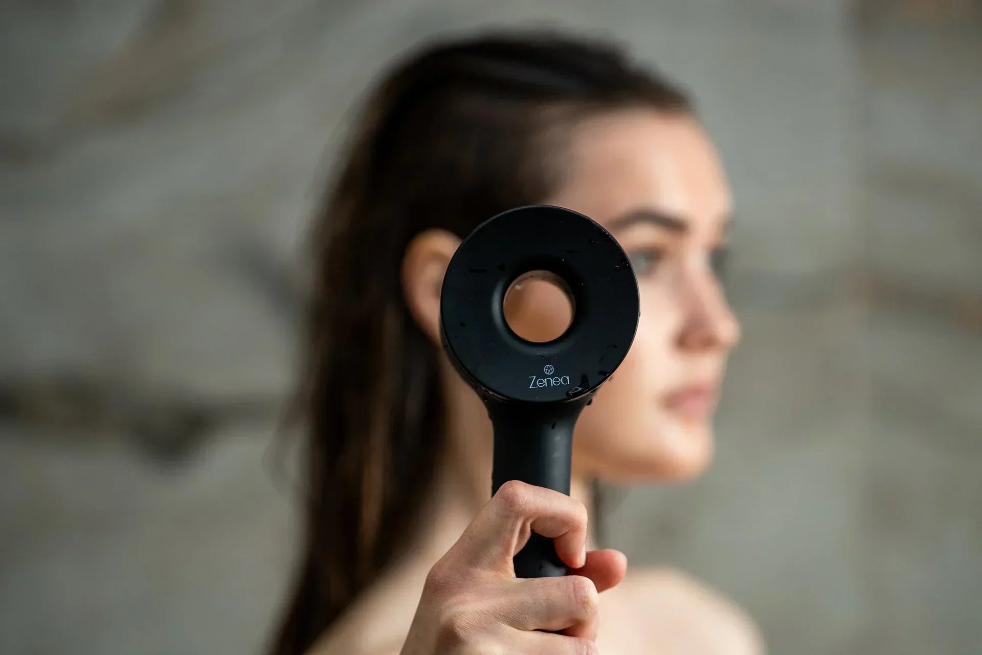 Žena drží čiernu filtračnú sprchovú hlavicu Zenea pred sebou v kúpeľni